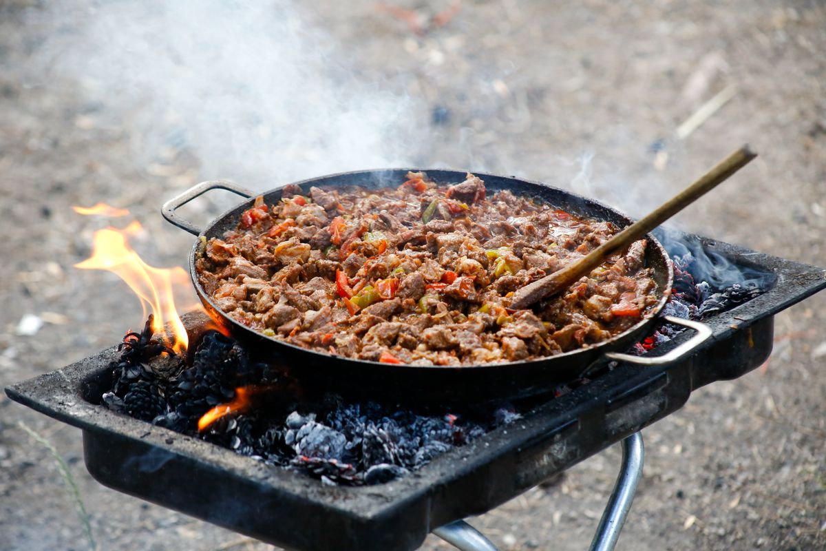 Delicious BBQ meat cooked outdoors on an open fire grill with vibrant peppers.