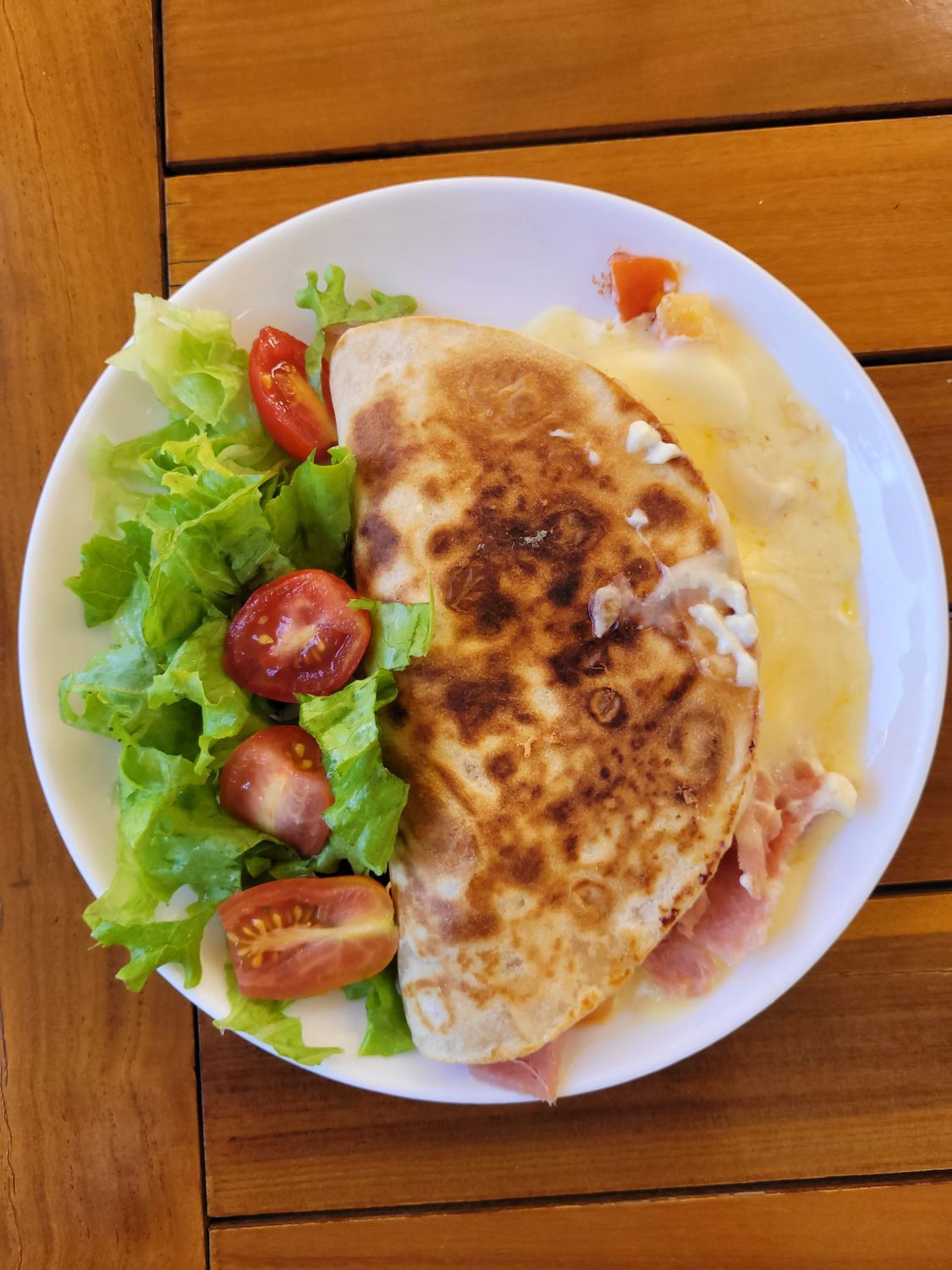 Delicious cheesy quesadilla with fresh lettuce and tomato salad on a wooden table.