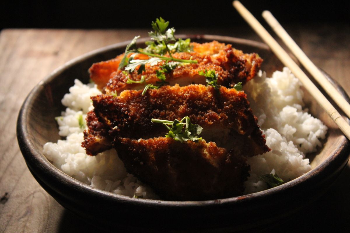 Delicious crispy fried chicken katsu served on a bowl of fluffy white rice with fresh herbs.