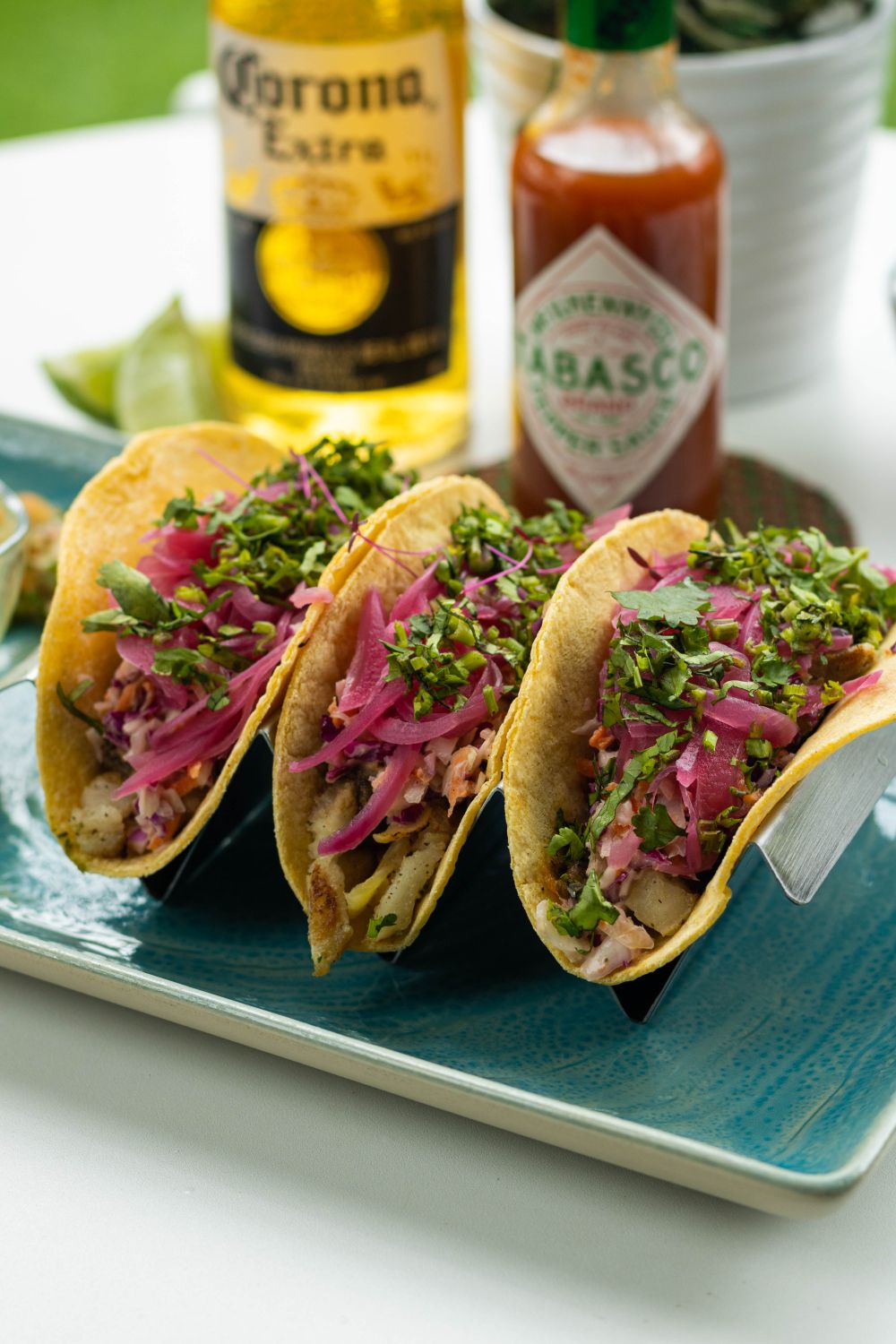 Delicious Mexican tacos on a tray with Tabasco sauce and beer in the background.