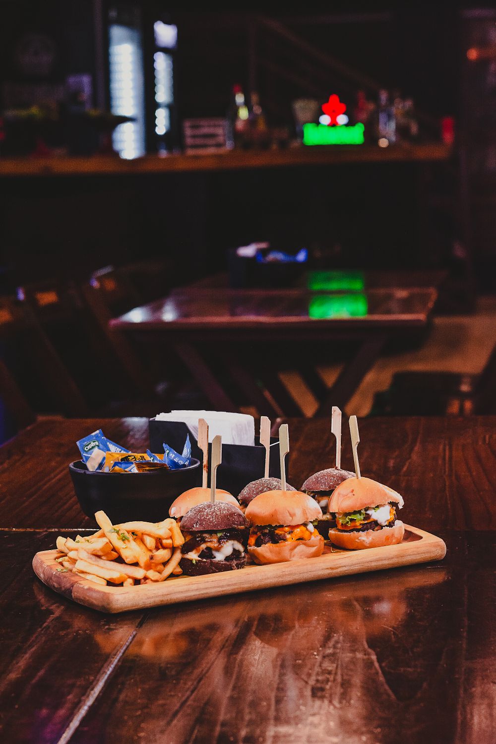 Delicious mini burgers with fries and chips on a wooden tray, perfect for food lovers in an indoor restaurant setting.