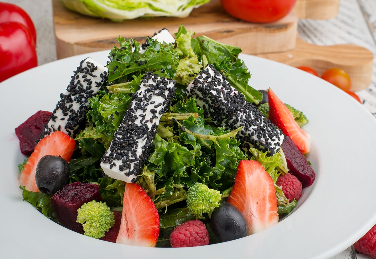 Fresh mixed green salad topped with black sesame cheese and colorful fruits, perfect for a healthy meal.