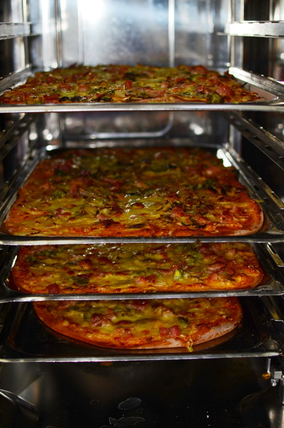 Freshly baked pizzas in an industrial oven, topped with green peppers and cheese.