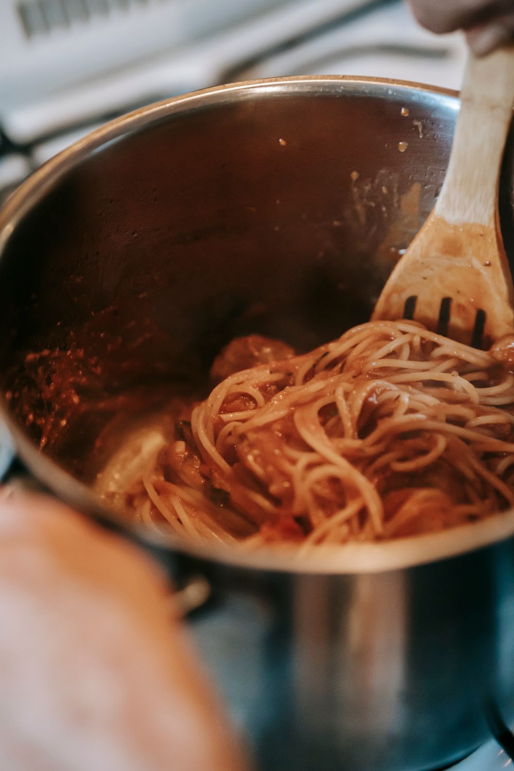 From above of appetizing homemade spaghetti with tomato sauce and meatballs in metal saucepan placed on stove in kitchen