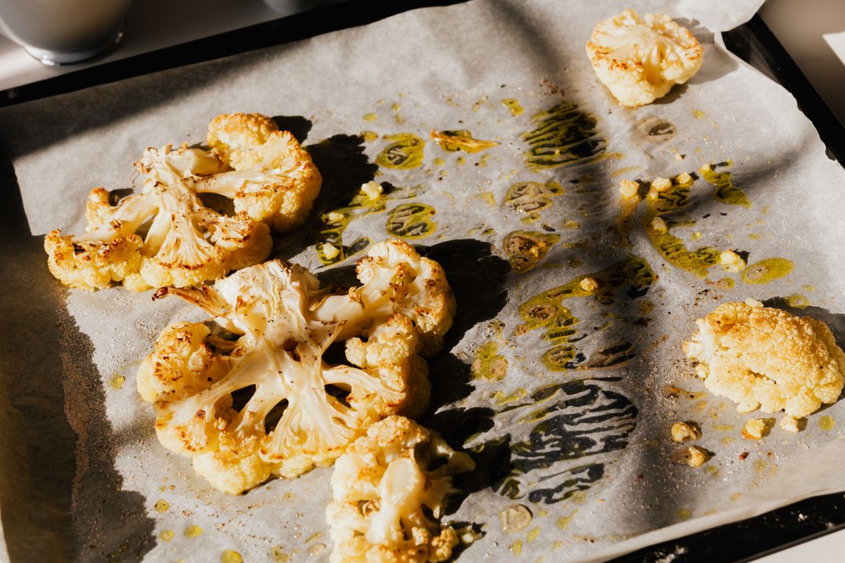 Golden roasted cauliflower slices on baking paper, seasoned with herbs and olive oil.