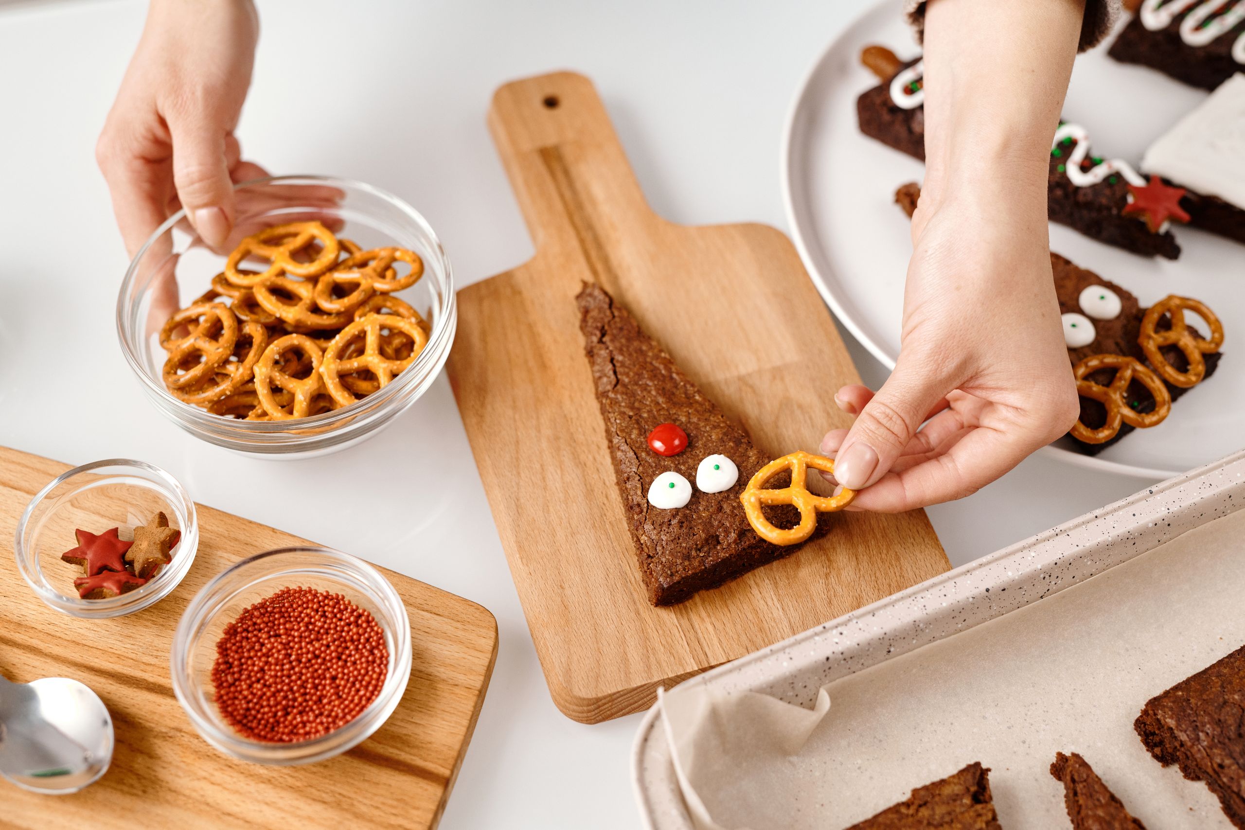 Hands decorate Christmas brownies with pretzels and icing, perfect for holiday treats.