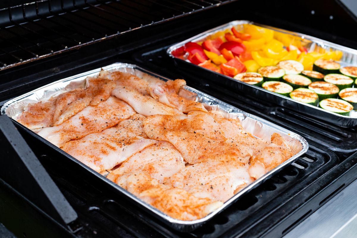 7 Family Dinners Everyone Might Actually Enjoy. 1 Juicy seasoned chicken and fresh vegetables grilling in aluminum trays for a delicious meal.