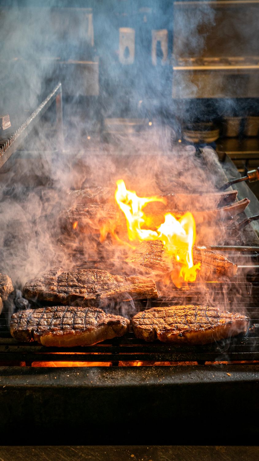 Juicy steaks grilling with intense flames and smoke, capturing a perfect barbecue scene.