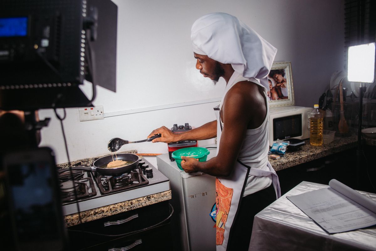 Man in apron and chef hat cooks in home kitchen with professional lighting setup.