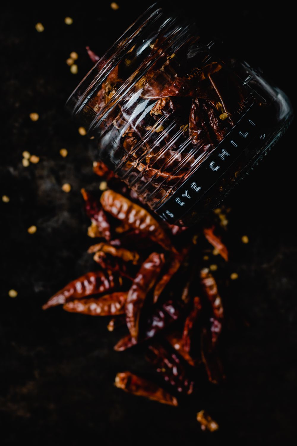 Five Dried Chilis That Will Change the Way You Cook, No Spice Packet Required 2 Overturned glass jar spilling dried red chili peppers on a dark surface, highlighting spicy flavor.