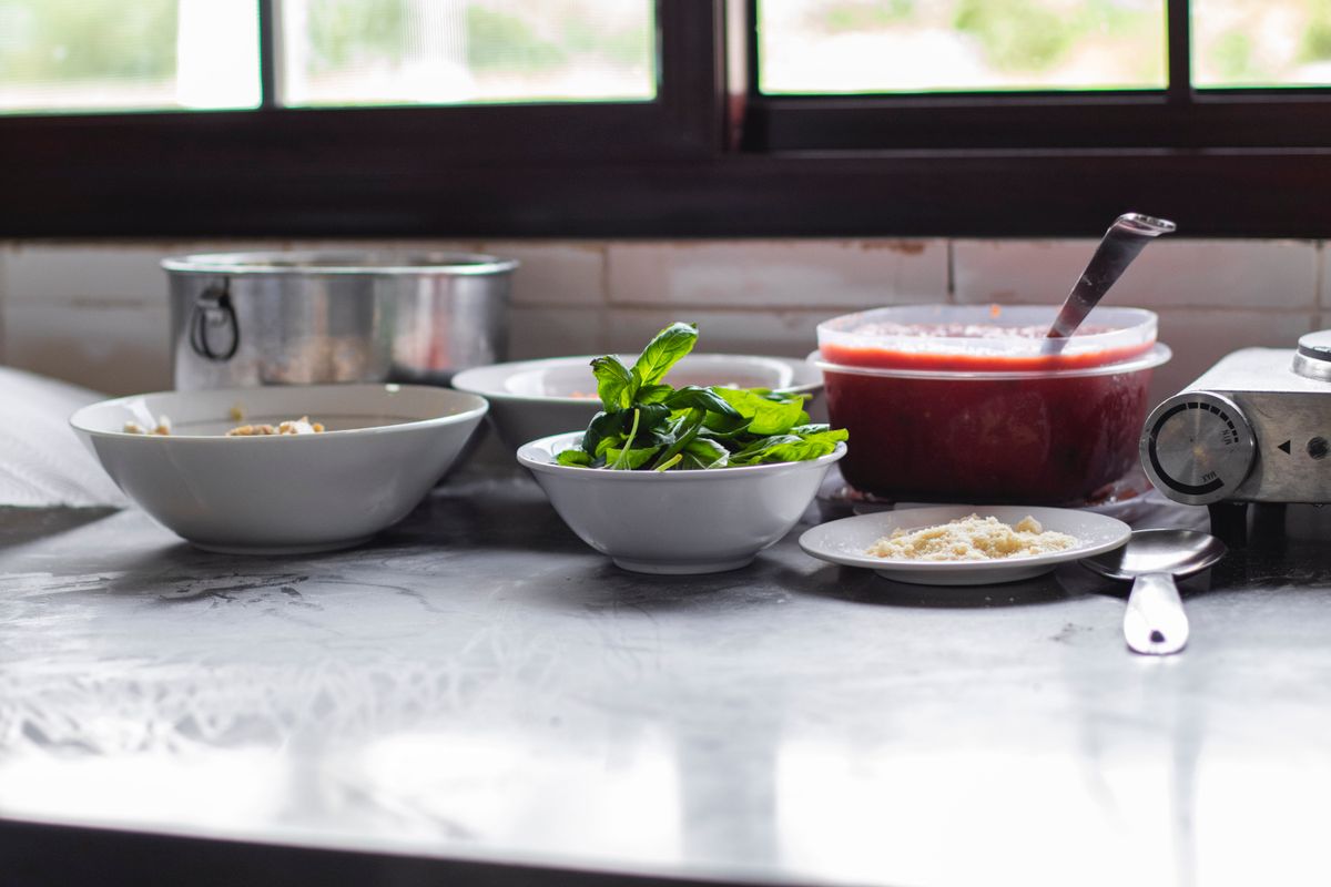 Preparation scene with fresh basil, parmesan, and tomato sauce on a kitchen counter.
