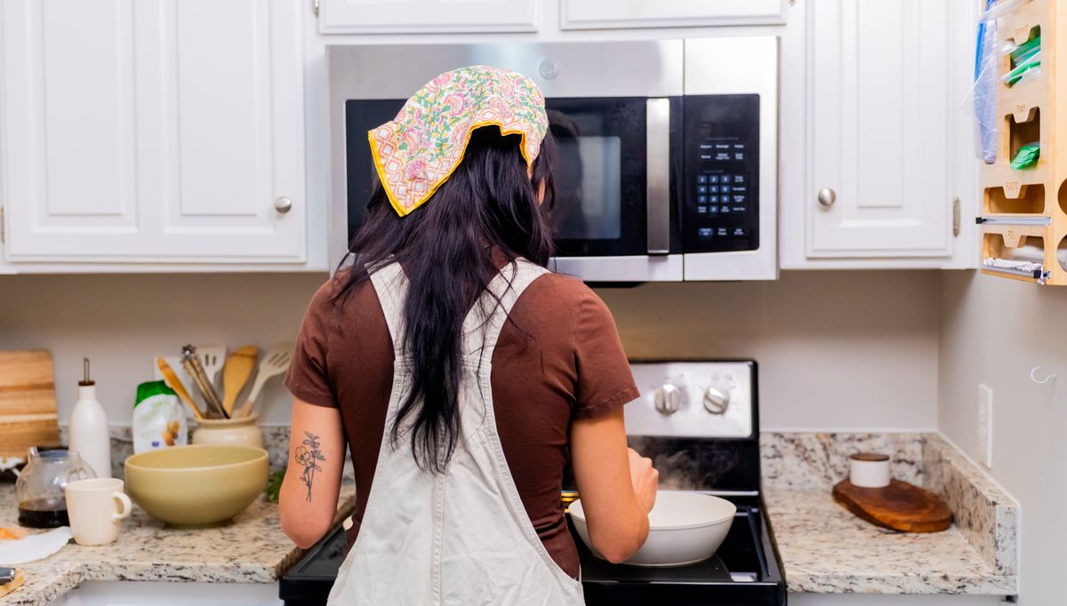 Rear view of a woman cooking in a modern kitchen with white cabinets and granite countertops.