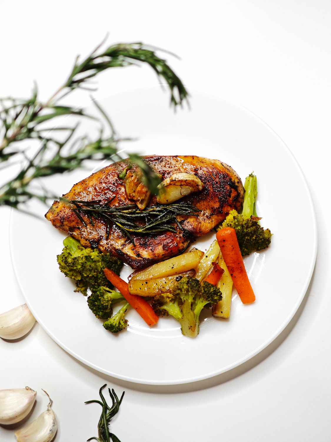 Savor roasted chicken with rosemary, garlic, and mixed vegetables on a white plate.