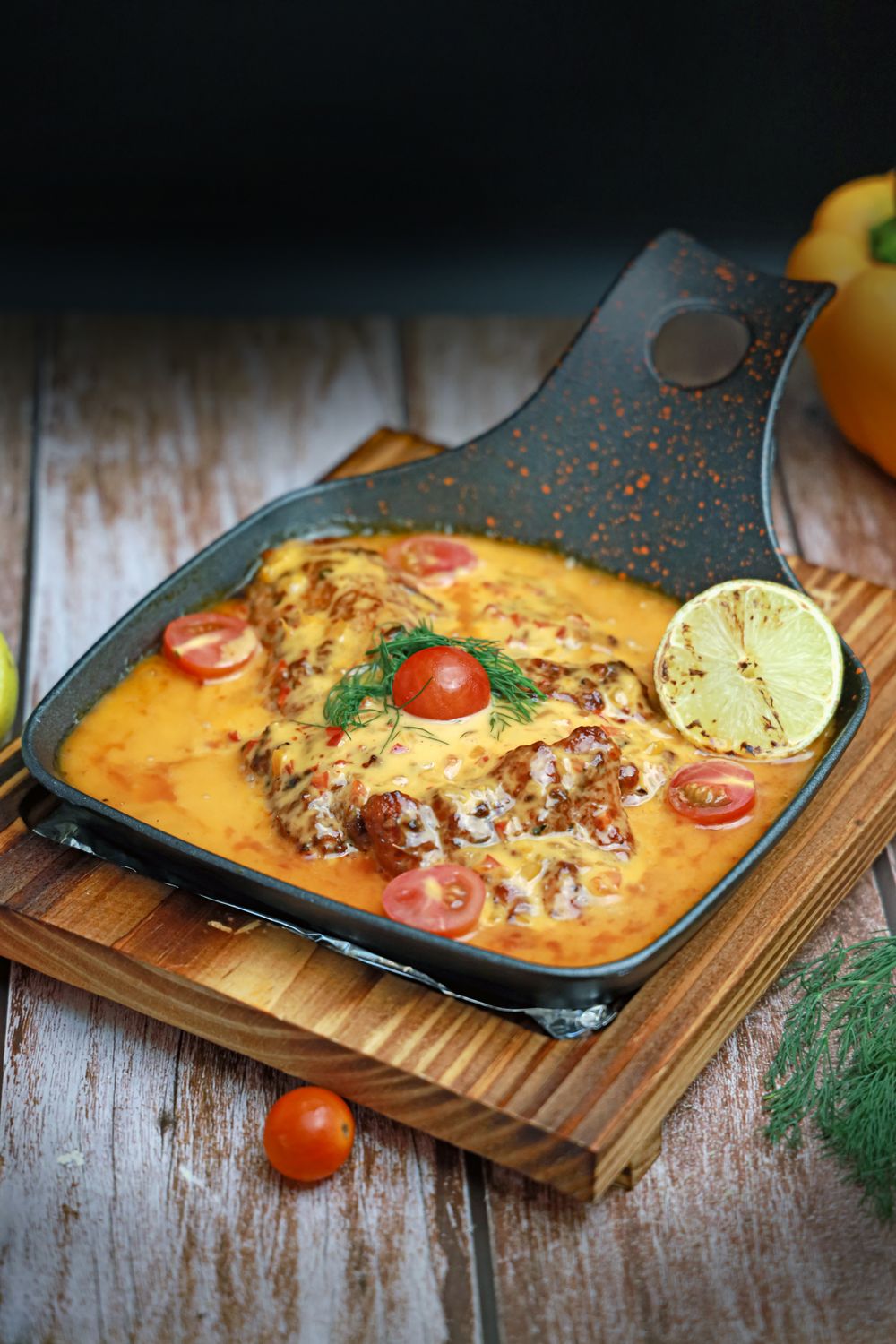 Skillet-cooked grilled chicken with creamy tomato sauce and herbs on a rustic wooden board.