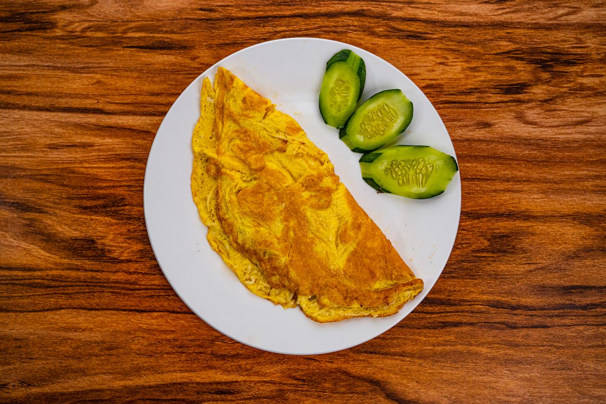 Top view of a delicious egg omelette served with fresh cucumber slices on a white plate.