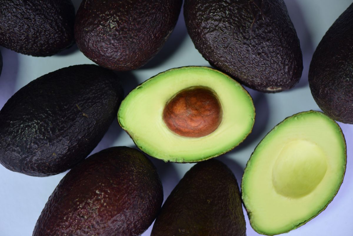 Top view of fresh avocados and cut halves on a white surface, showcasing their vibrant green color.