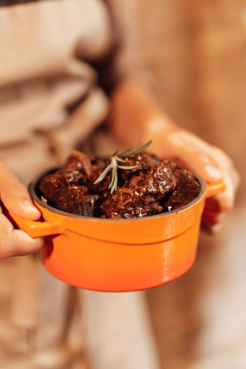 Warm and savory beef stew garnished with rosemary, served in a vibrant orange pot.