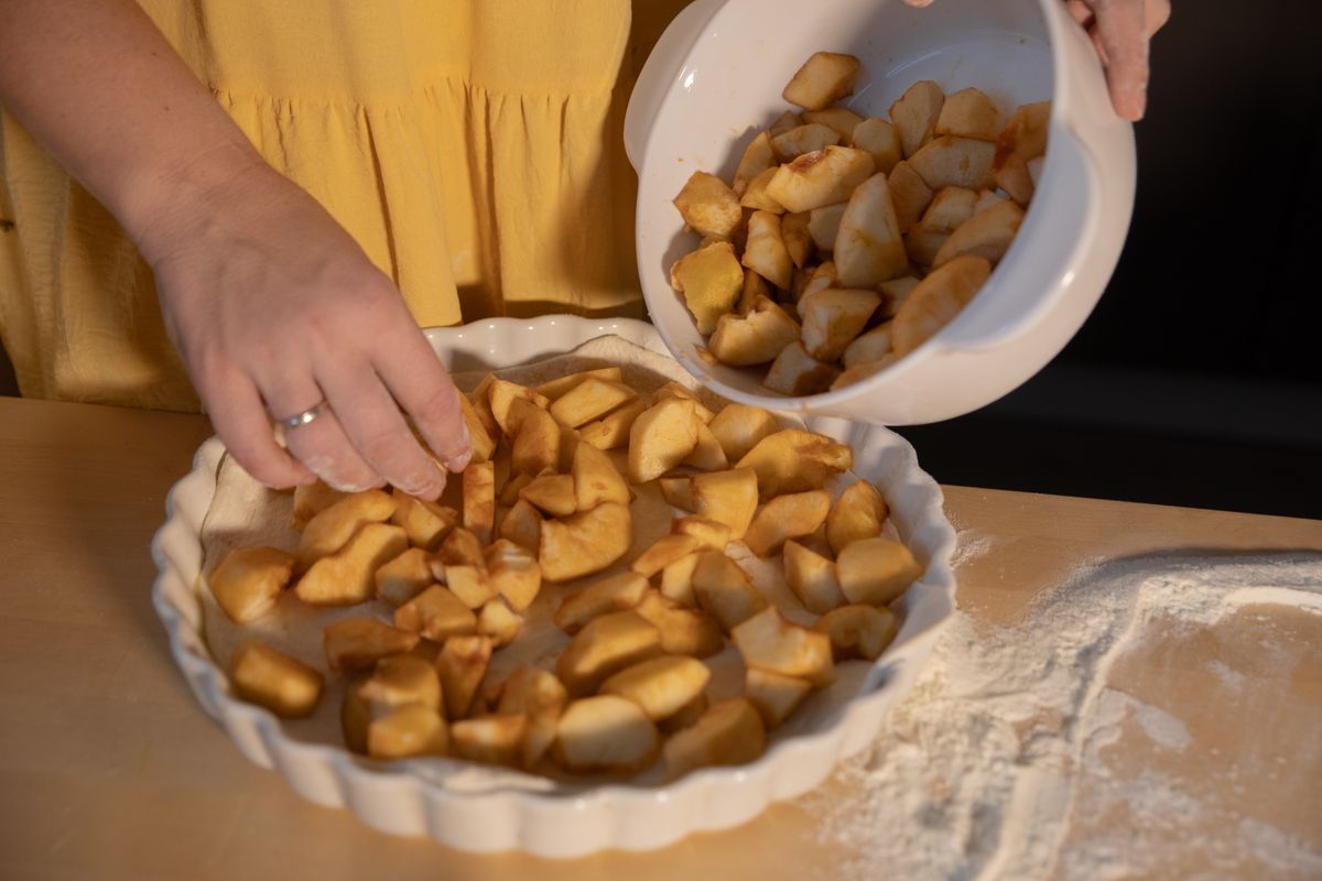Woman adds sliced apples to pie crust, creating a delicious homemade dessert.