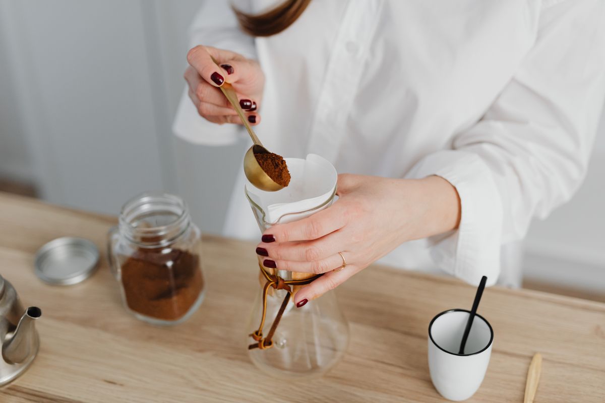 The Exact Amount of Coffee to Drink to Avoid Anxiety and Jitters but Still Get the Benefits 1 Woman in white shirt making pour over coffee on wooden surface.