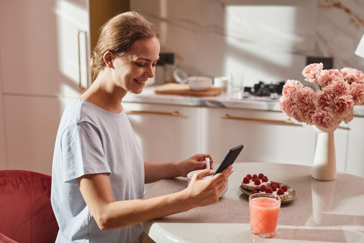 Woman smiling while using phone at breakfast with raspberries and juice