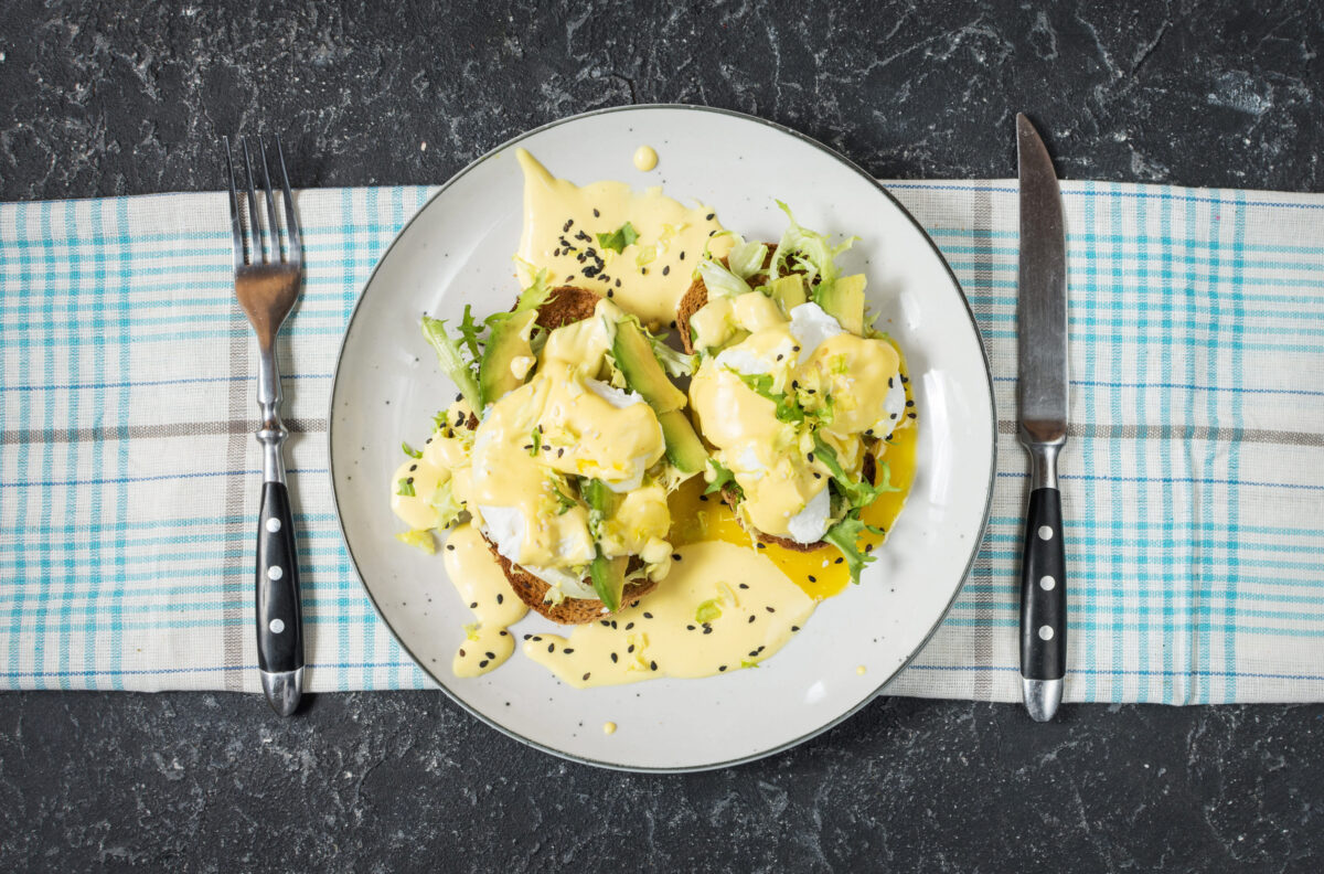 Eggs Benedict with salad and avocado on stone background. Top view