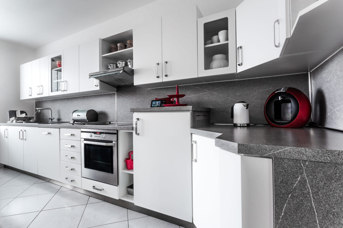 10 Things Every '90s Kitchen Had 2 Kitchen at home in classic style, decorated in white with marble fittings and with numerous accessories and appliances in stainless steel or in dark red color. Floor is lined with white square tiles.
