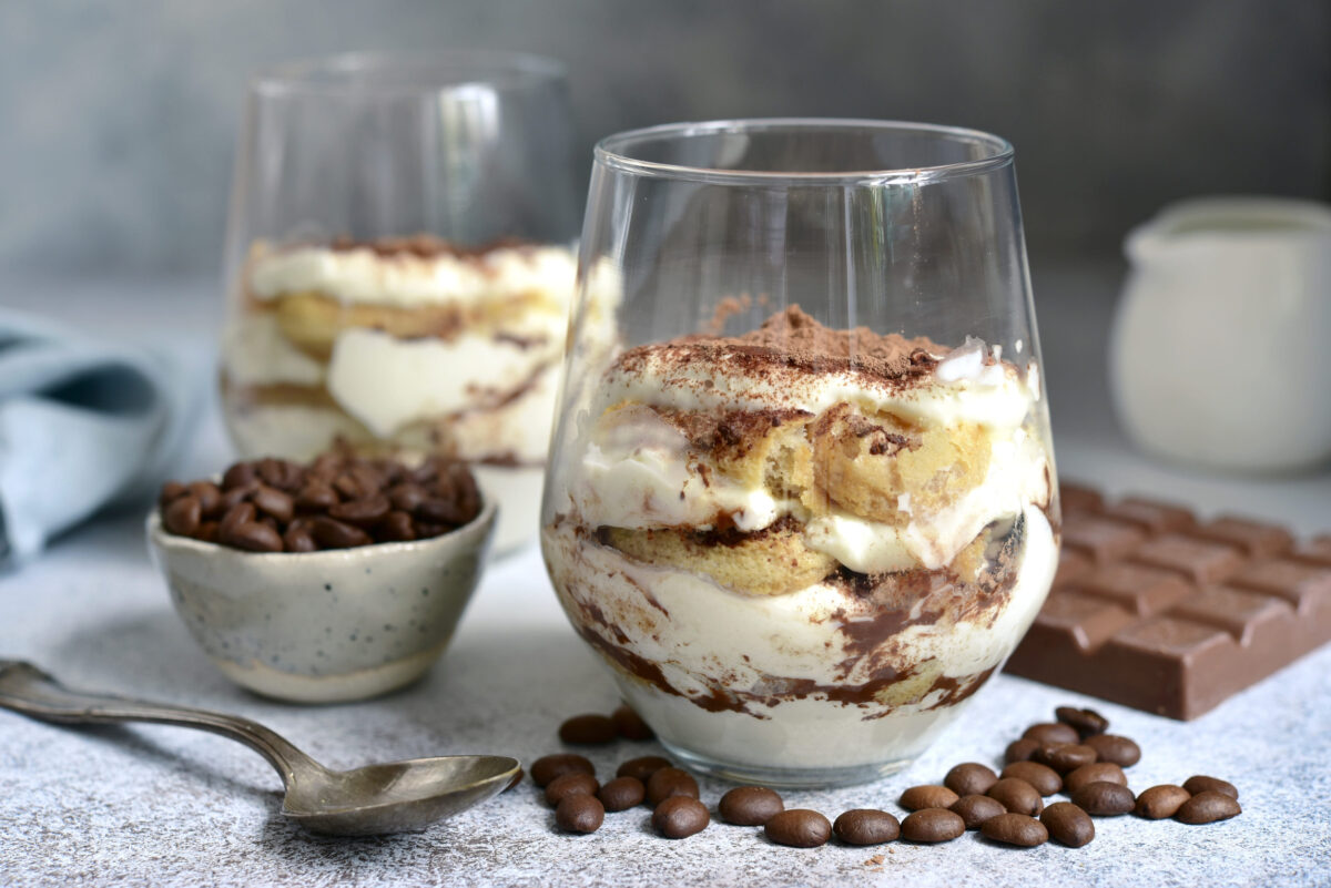 Tiramisu - traditional italian coffee dessert with biscuits and mascarpone cheese in a glass on a light slate,stone or concrete background.