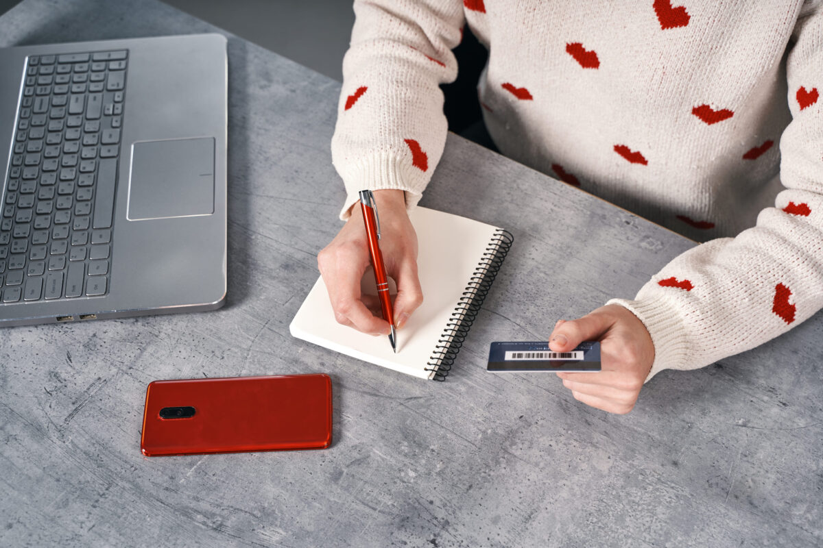 10 Things You Should Think Twice About Carrying in Your Wallet After 50 2 Woman hands writing in notepad and holding bank card. Shopping online concept