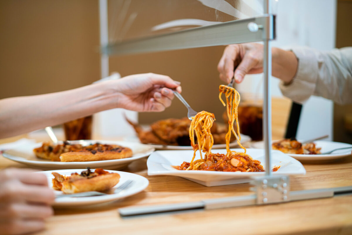 Asian woman eating food while siting separate and keep distance with table plastic shield partition in restaurant, new normal, restaurant, coronavirus outbreak and social distancing concept