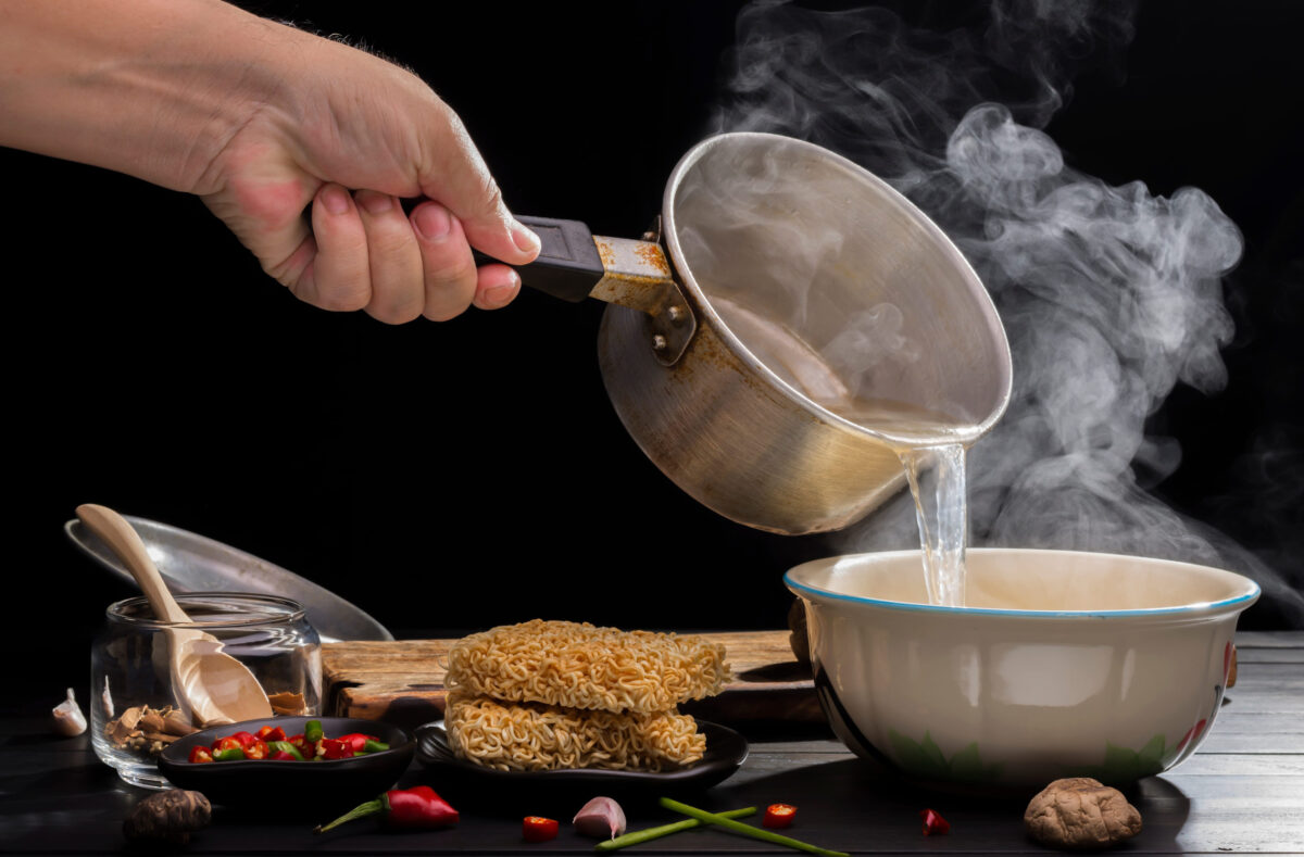 Chef is preparing hot soup noodles with seasoning with shiitake mushrooms chili and lime on wooden table