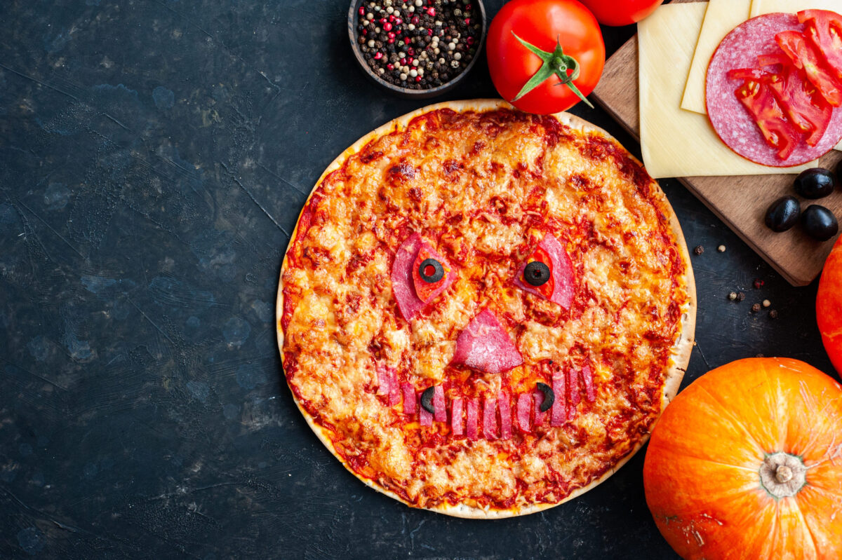 Pumpkin pizza for a Halloween party on a dark background. Pizza decorated with a scary face. Childrens holiday food.