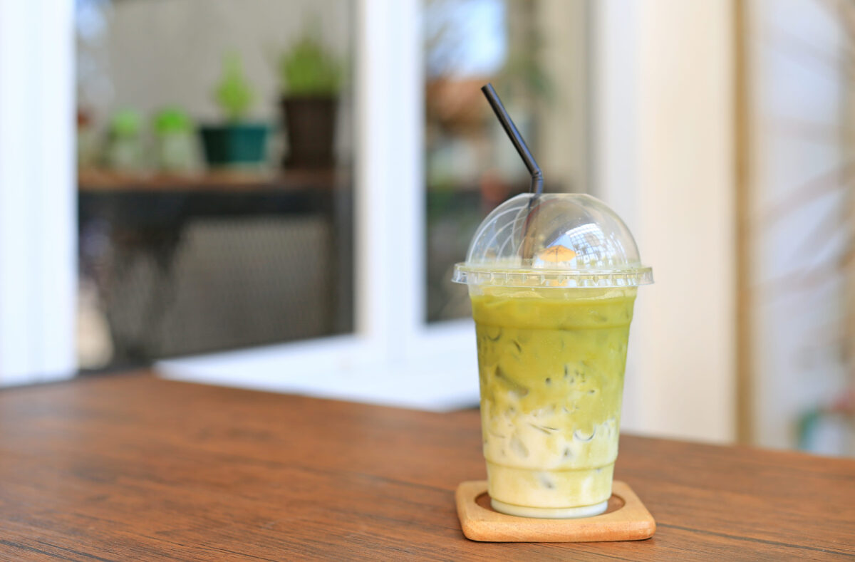 Iced matcha green tea latte with milk with brown straw in take away cup on wooden table at cafe.