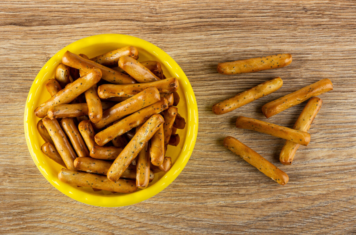 10 Restaurants Where the Side Dish Became Just as Famous as the Main 2 Breadsticks with poppy in yellow plastic bowl, breadsticks on brown wooden table. Top view