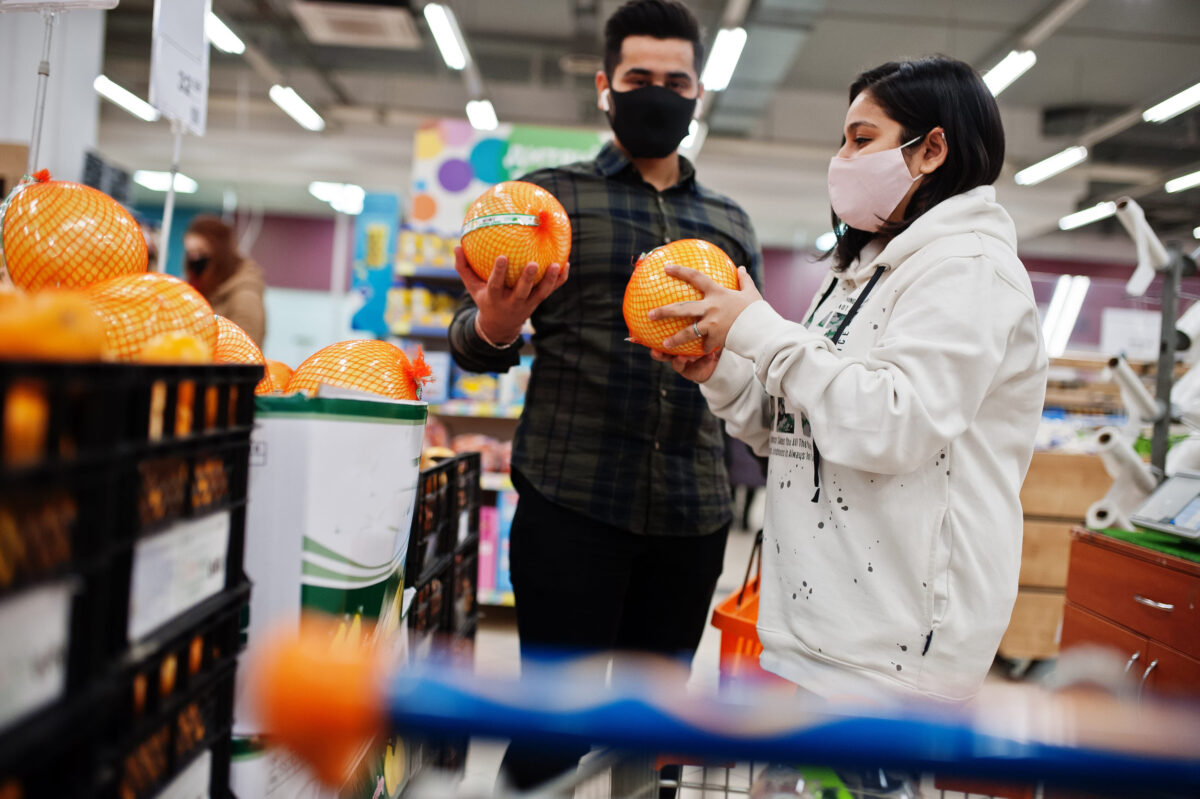 Asian couple wear in protective face mask shopping together in supermarket during pandemic. Choose pomelo fruits.