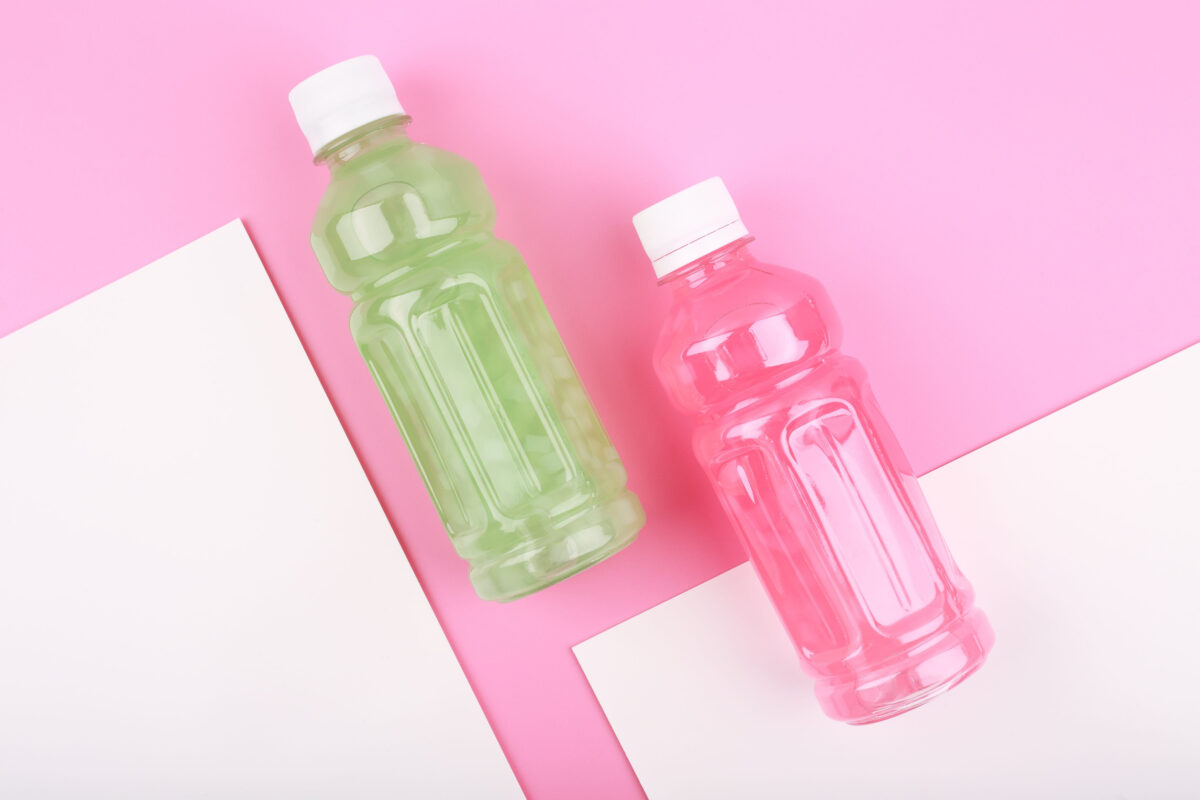 Flat lay with pink and green drinks in transparent plastic bottles against pink background with white sheets of paper
