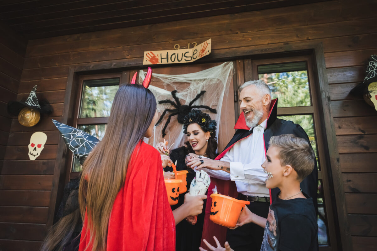 excited family in halloween costumes holding buckets with candies on house porch
