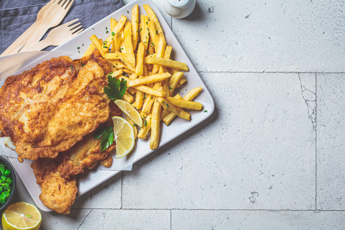 Fish and chips with green peas on a gray tile background, top view, copy space. British cuisine concept.