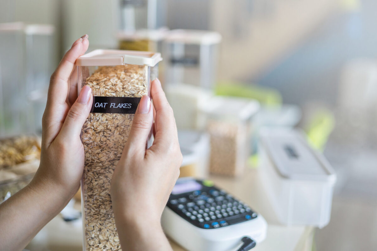 Closeup female hands applying printing sticker with oat flakes title on transparent plastic case