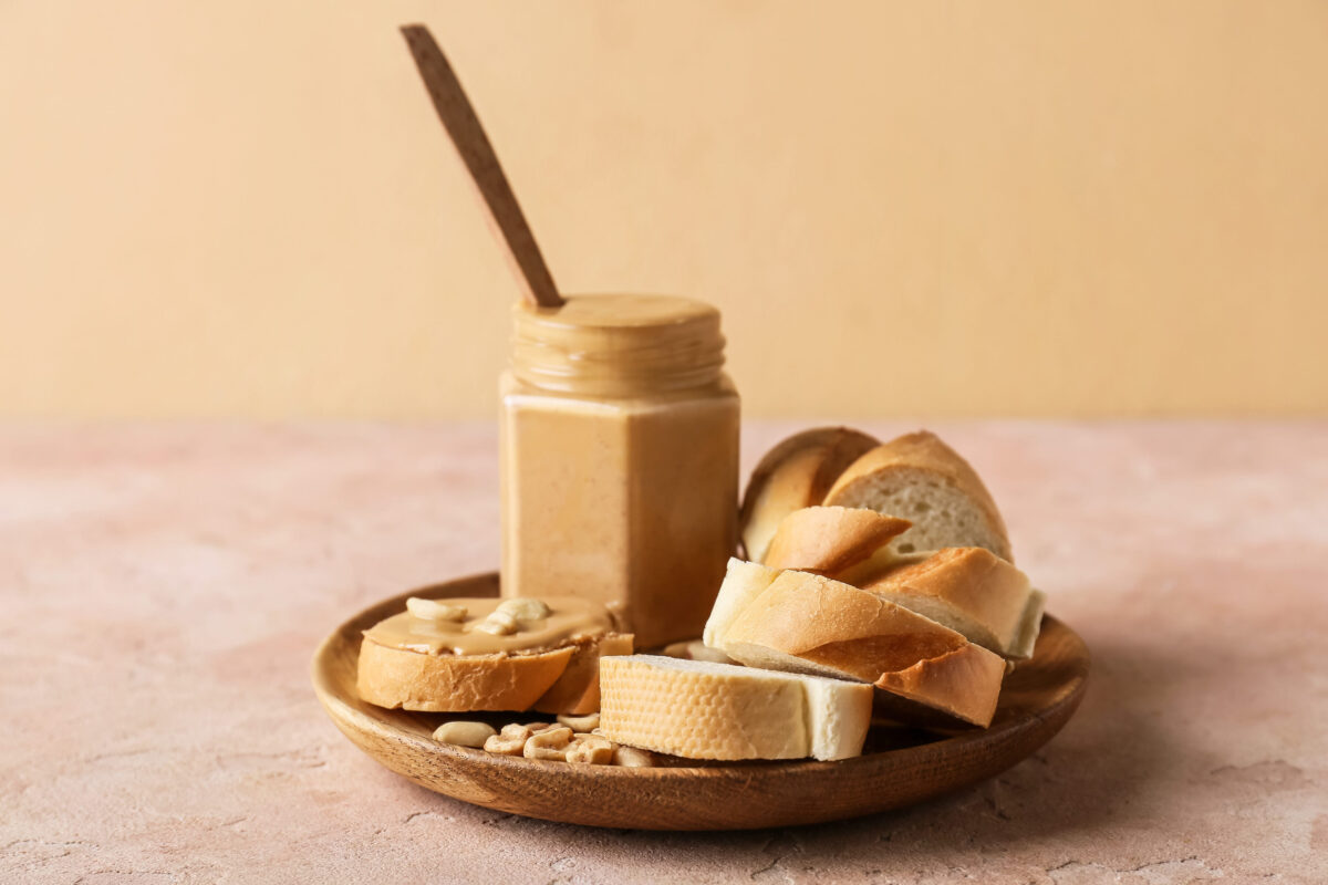 Jar with tasty peanut butter and bread on color background