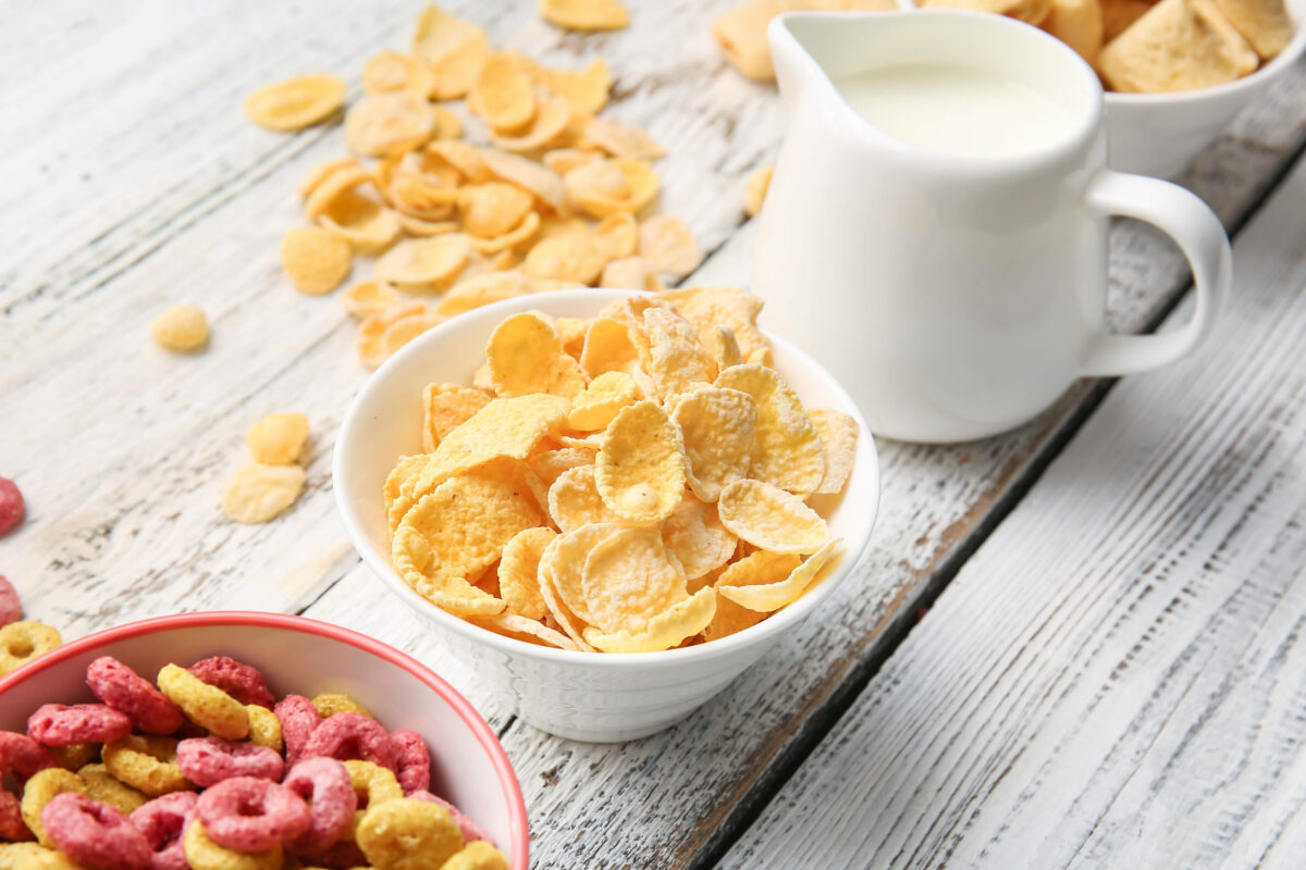 Bowls with different cereals and milk on light wooden background, closeup