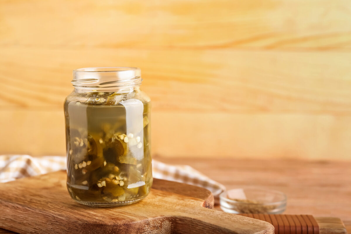 Glass jar with canned jalapeno on wooden background