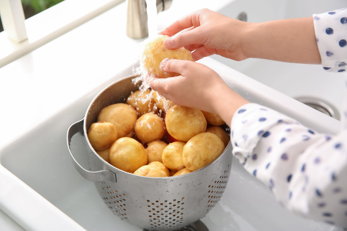 Woman washing fresh potatoes in kitchen sink, closeup