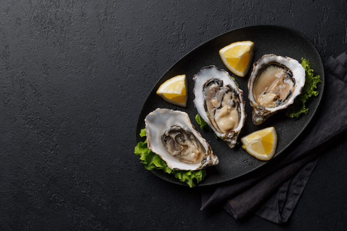 Fresh oysters with lemon on plate. Flat lay with copy space