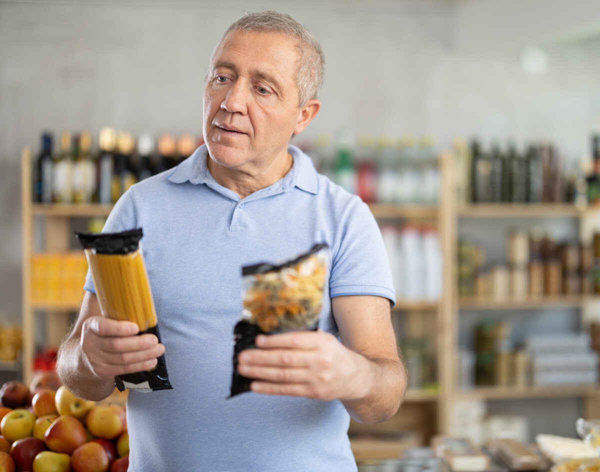 Mature man choosing package of pasta in grocery store