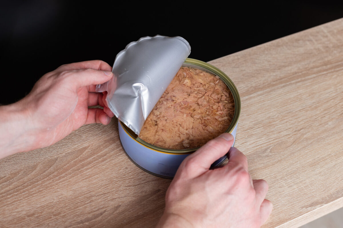 A man opens a big can of tuna. Closeup.