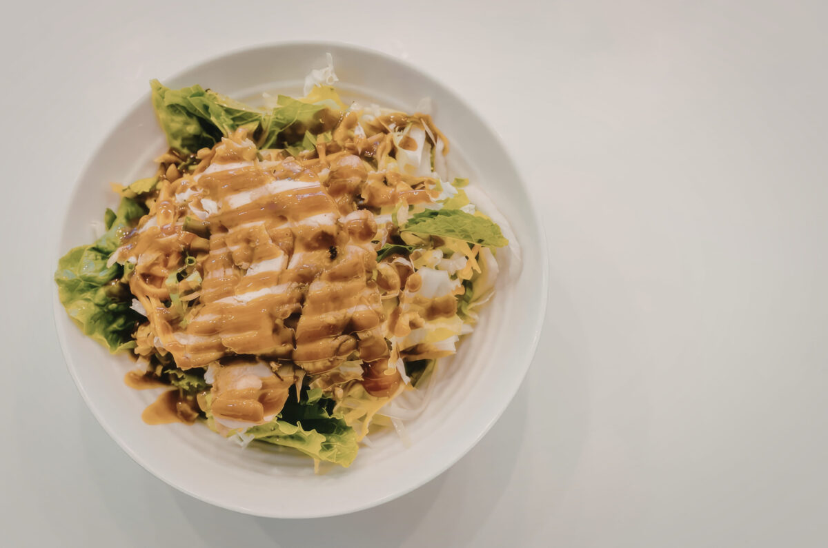 A white plate containing a salad with mixed greens, chicken, and a drizzle of orange sauce.
