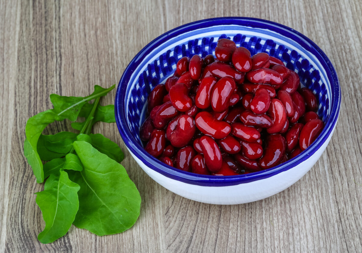 Kidney beans in the bowl with ruccola leaves on wood background