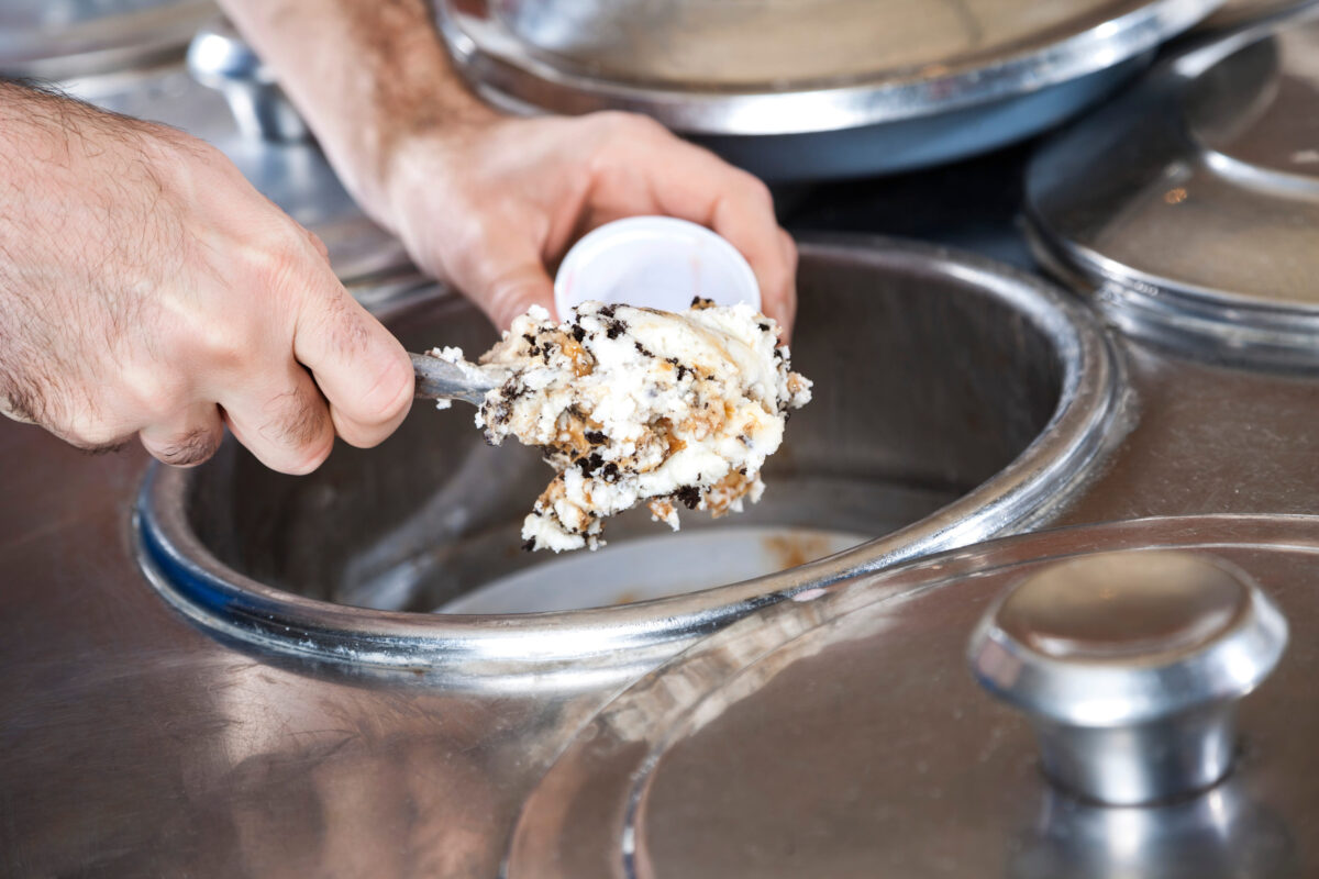 Closeup of waiter's hands filling butterscotch ice cream with spatula in cup at parlor
