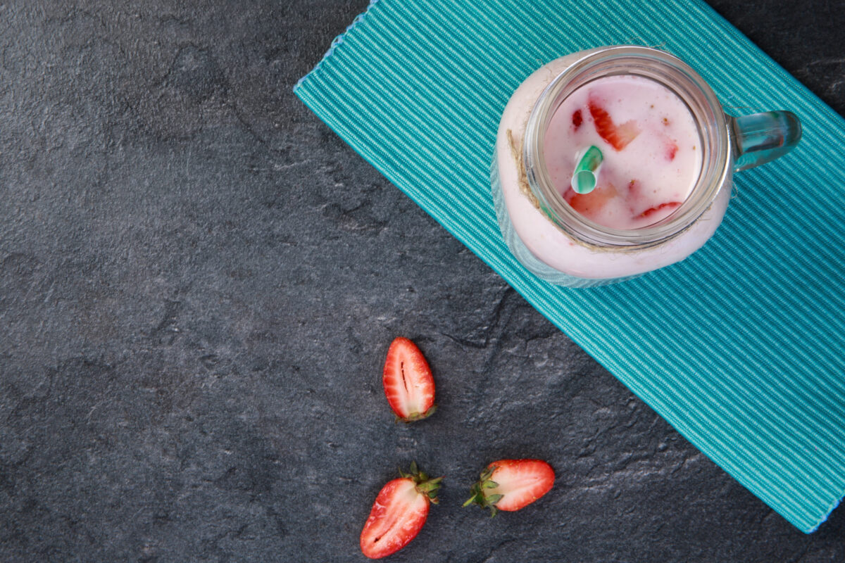 A top view on a mason jar with tasty fresh jogurt and three pieces of strawberries on a marble background. Close-up of drink. Food concept.