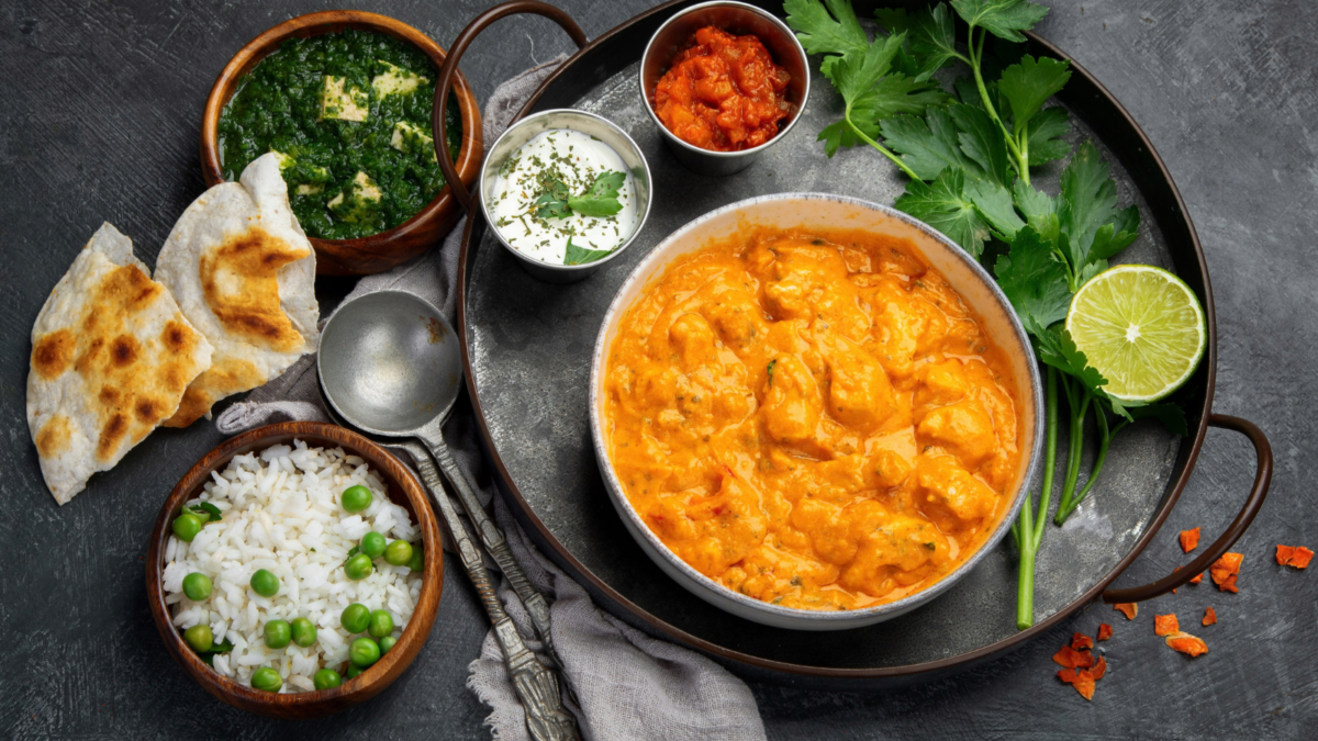 A delightful spread of traditional Indian cuisine featuring creamy butter chicken, fragrant rice, and vibrant accompaniments like fresh cilantro and lime. Perfectly paired with crispy naan and a side of sautéed greens, this meal offers a feast for the senses, inviting everyone to savor the rich flavors and colorful presentation. Image Credit: baibakova/ 123RF